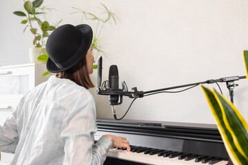 European woman hipster in a hat plays the piano and sings, recording music and song or podcast,...