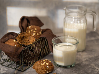 In the photo there are cookies in a vase. On top of the cookies are sprinkled with white sesame seeds. Nearby, there is milk in a jug and a glass. Beautiful white-brown colors. Morning breakfast.
