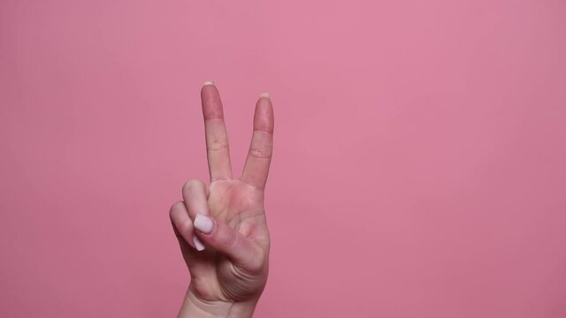 Woman's hand shows a sign of peace or victory on a pink background, close-up