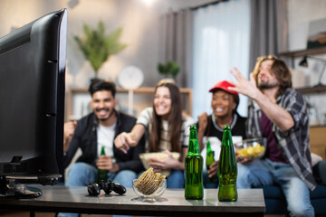 Emotional men and women giving high five for celebrating score of favorite football team during championship. Multi ethnic friends sitting on couch and watching match on TV.