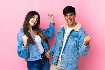 Young couple over isolated pink background celebrating a victory