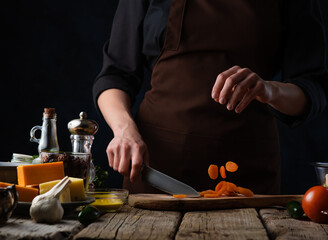 The chef in the photo is slicing carrots on a cutting board. Levitation. In the left corner of the photo there are many ingredients - garlic, beaten eggs in a bowl, cheese, soy sauce, spices.