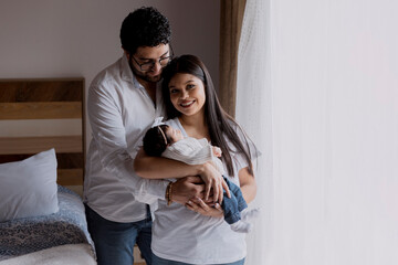 mother and father smiling while holding their newborn baby in their arms - happy young Hispanic parents with their newborn baby