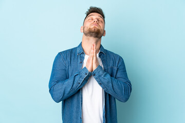 Russian handsome man isolated on blue background keeps palm together. Person asks for something