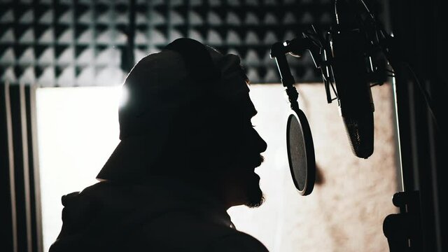 Side view of young rapper performing song in sound recording studio singing into microphone. Concept for hobby, talent and performance.