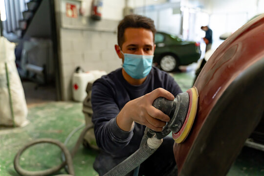 Young worker sands the bumper of a vehicle with his machine. Madrid.
