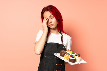 Pastry chef holding a muffins isolated on pink background with headache