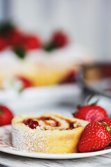 Homemade strawberry shortcake cake roll or Roulade with a berry jam filling and powdered sugar with mint leaves. Dessert over a white rustic table. Selective focus with blurred foreground  background