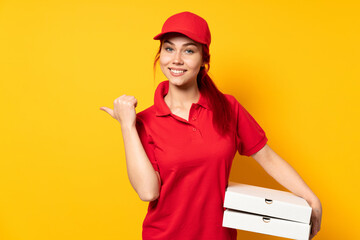Pizza delivery girl holding a pizza over isolated background pointing to the side to present a product