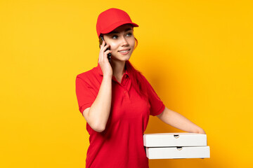 Pizza delivery girl holding a pizza over isolated background keeping a conversation with the mobile phone with someone