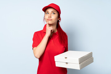 Pizza delivery girl holding a pizza over isolated background having doubts while looking up