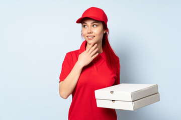 Pizza delivery girl holding a pizza over isolated background looking up while smiling