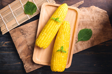 Sweet corn cob on wooden plate and wooden background, Top view