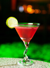 A red Martini cocktail on a green background.
