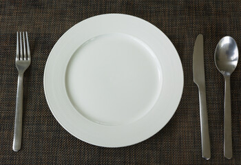 Close up and selective focus shot of tableware (white plate, fork, spoon and knife) on table in restaurant which is well prepared and decorated for lunch and dinner meal or food.