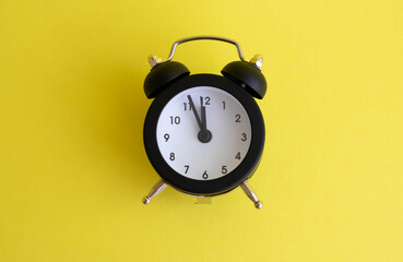 Black vintage alarm clock lying on a yellow backgroun