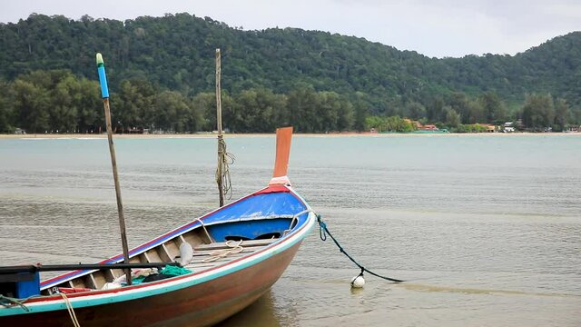 Thai longtail boat anchored along the beach by rope on the island of Koh Lanta in Thailand with water and waves.