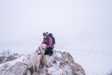 Fototapeta na wymiar Portrait of tourist female standing on the edge of cliff over frozen sea with white dog. Winter hike in Siberia
