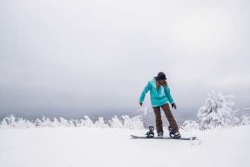 Snowboarder female putting on one leg in snowboard preparing to slide down slope in winter ski resort