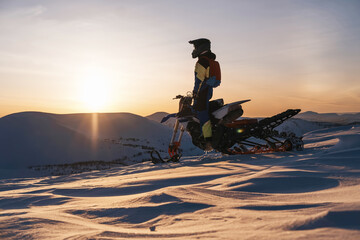 Snowbike rider female standing on top of mountain during sunset with atmospheric landscape view....