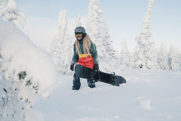 Fototapeta na wymiar Female snowboarder wearing long dreadlocks and ratsa hoody in white winter forest walking in snow powder