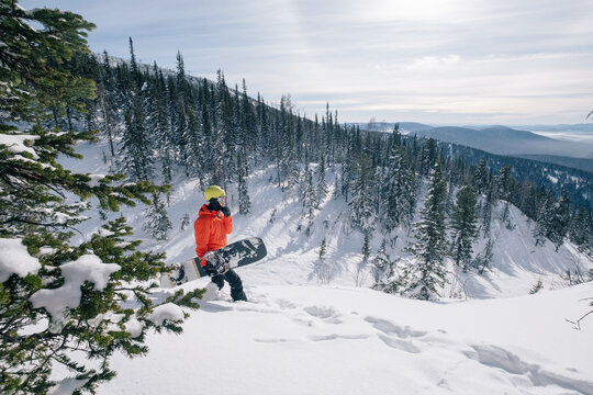 Snowboarder freerider walking ski touring in forest, wild mountains, winter sunny day