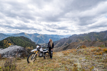 Fototapeta na wymiar Young woman motorcyclist enjoying and rest on the mountain top with her enduro motorcycle. Off road motor traveling in wild mountains