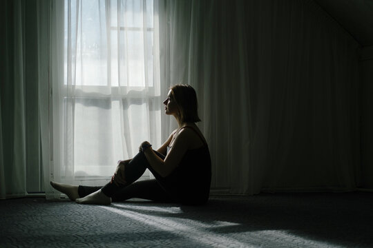 Silhouette of pretty young woman sitting on the floor near big window