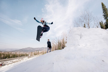 Snowboarder female jumping from kicker in winter sunny day