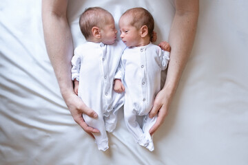 Newborn twins on the bed, in the arms of their parents, on a white background. Life style, emotions of kids. - obrazy, fototapety, plakaty