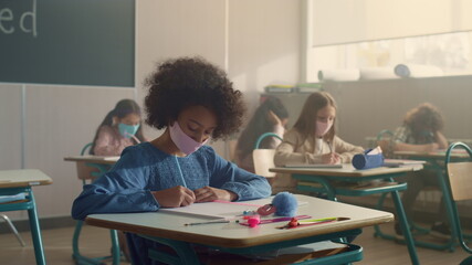 Children in face masks studying in classroom during coronavirus pandemic