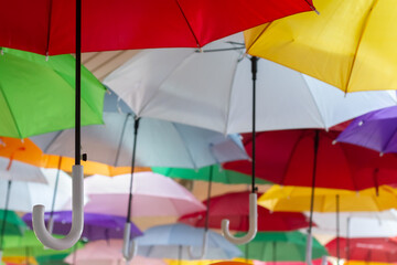 Low angle view group of colorful umbrellas hanging on wooden plank ceiling background. Selective focus at the left crook handle.