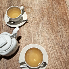 Two cups of tea on white saucers and a teapot are on a wooden table.