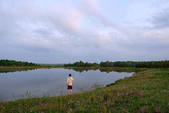 Scenery. Summer, lake. On the green shore is a man in shorts and a sweater, view from the back.