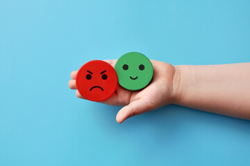 Mugs with an evil and kind face in the hands of a child. Negative and positive emotions of the child