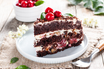 A piece of chocolate cake with cherry on plate on a wooden table.