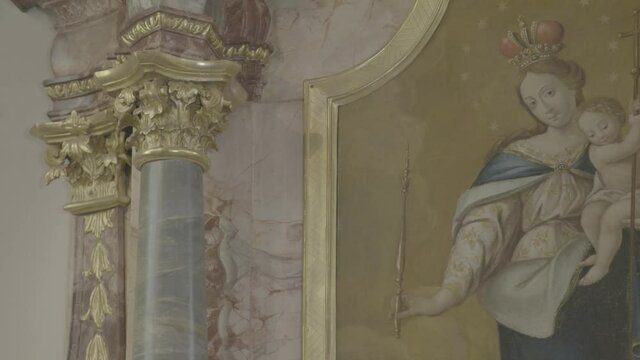 Camera pans to the Virgin Mary with Jesus on her arm on a painting on a baroque altar