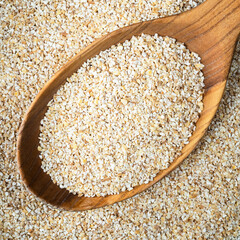 crushed pot barley groats in wooden spoon closeup