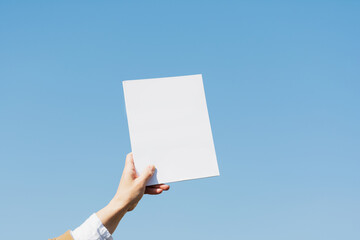 A female hand holds a book in a white cover on a blue background.