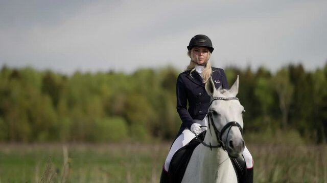 A female professional jockey riding a white horse gallops across a field