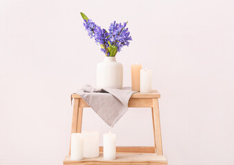 Vase with beautiful hyacinth flowers and burning candles on stand against color background