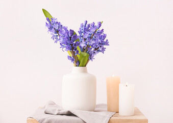 Vase with beautiful hyacinth flowers and burning candles on table against color background