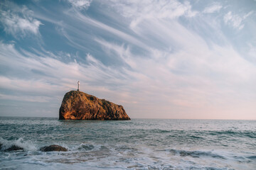 Bright sea sunset. The waves crash into the rock, lit by the warm sunset, sand and pebbles, volcanic basalt as in Iceland. Sea wave breaks into splashes and white foam. Never-ending beauty of nature
