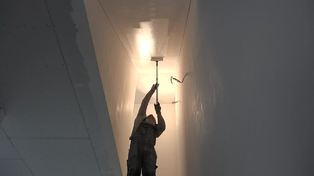 man painting gypsum plaster ceiling in staircase with painting roller