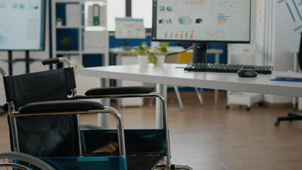 Wheelchair parked in empty office room near desk in start up financial company with disabled employee. Modern workspace with nobody in, computer with economic statisctics, corporate job