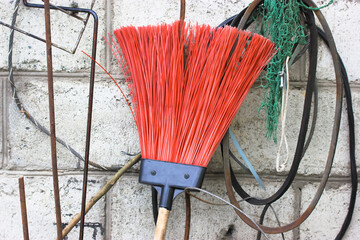 Fan rake with red tines to collect leaves, a rope against a wall on a backyard.
