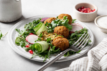 Falafel and fresh vegetables salad on a white ceramic plate on concrete background, selective focus. 