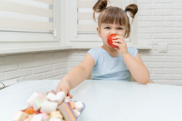 the girl eats a delicious ripe tomato and reaches for unhealthy sweets. healthy food selection concept