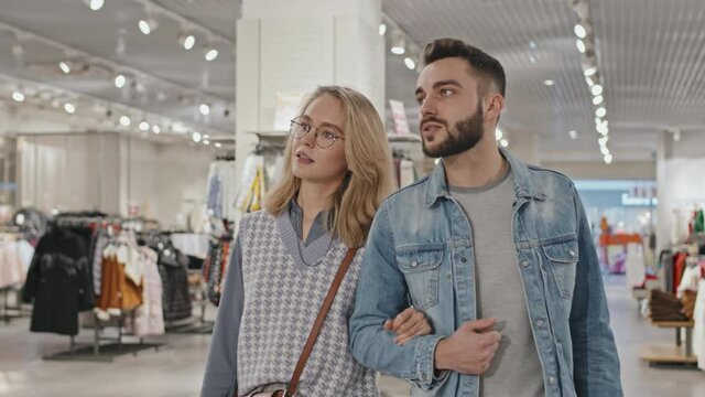 Medium shot of stylish young Caucasian couple talking while walking towards camera shopping in clothing store together