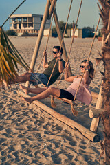 Young attractive couple swinging on seesaw on the beach.